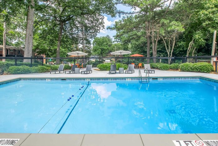 Inviting outdoor pool area with comfortable lounge chairs and umbrellas surrounded by lush greenery.