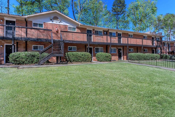 Charming brick apartment building with lush green lawn and inviting outdoor pathways.