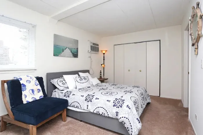 Bright and inviting bedroom with cozy bedding and stylish decor, featuring a plush chair and ample natural light.
