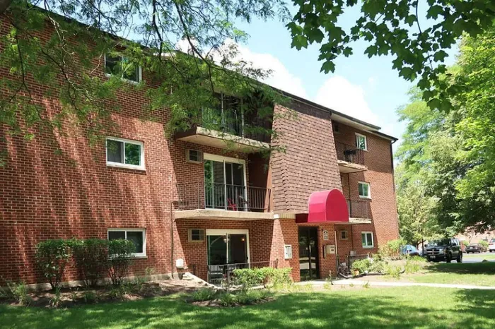 Inviting brick apartment building with balconies, surrounded by lush greenery and shaded by majestic trees.