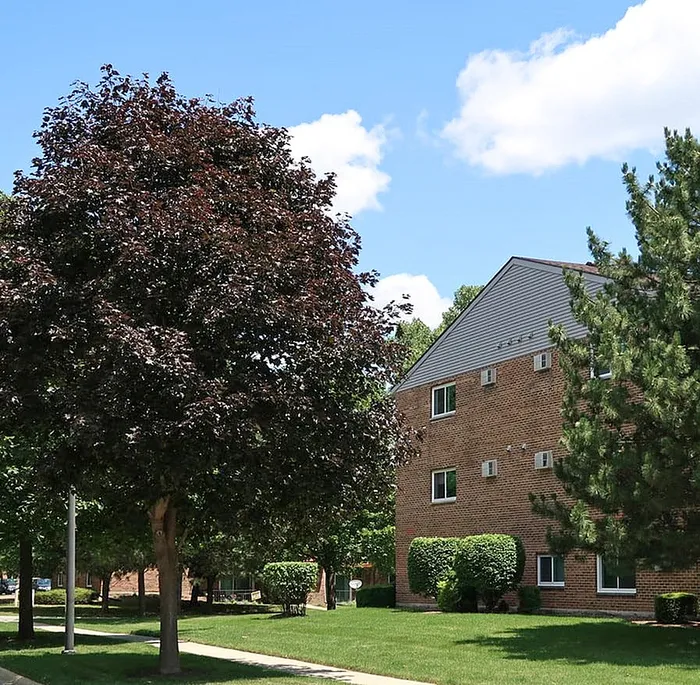 Charming apartment building surrounded by lush greenery and vibrant trees under a clear blue sky.