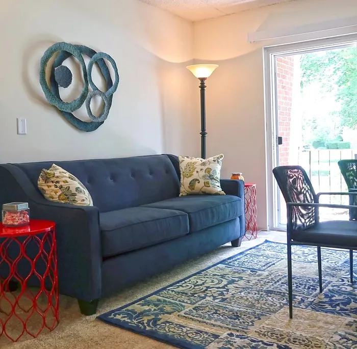 Inviting living room with stylish blue sofa, artistic wall decor, and a vibrant area rug, overlooking a serene outdoor view.