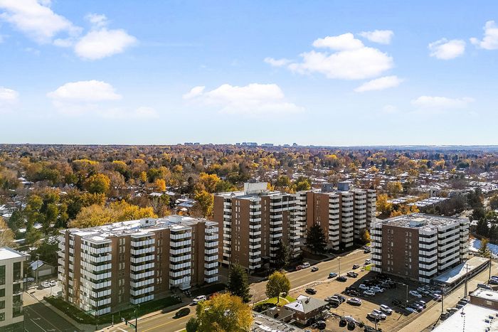 Stunning aerial view showcasing a modern apartment complex surrounded by lush, colorful trees under a bright blue sky.