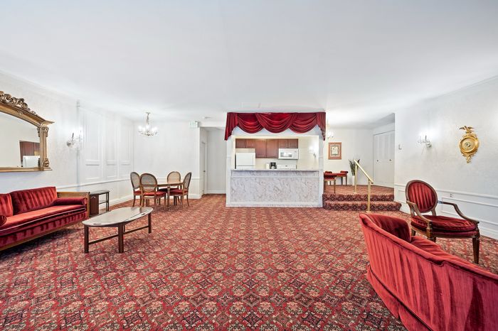 Elegant open-concept living space featuring plush red seating, a classic dining area, and a modern kitchenette with charming drapery accents.