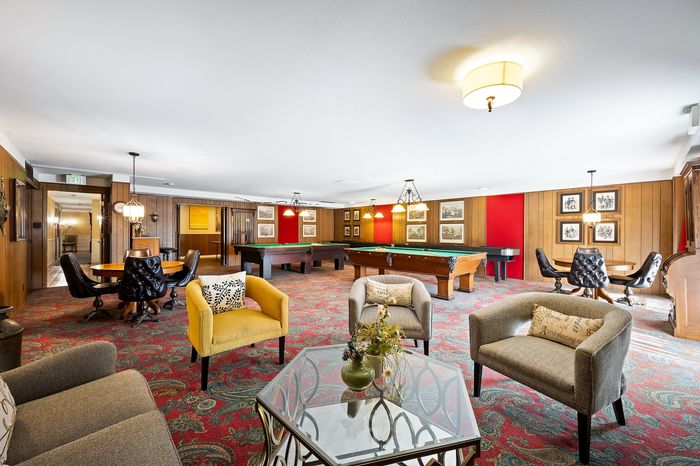Luxurious recreation room featuring classic wood paneling, elegant seating, and two stylish pool tables for entertainment.