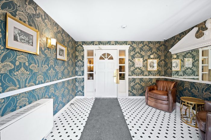 Charming apartment entryway with elegant patterned wallpaper, classic white door, and cozy leather seating.