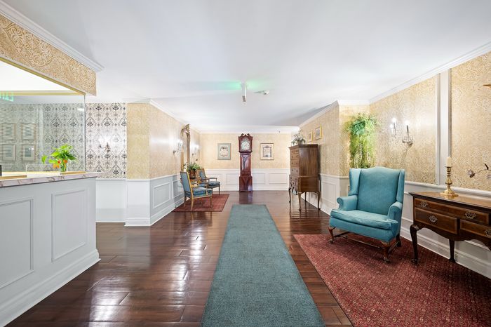 Elegant apartment lobby showcasing vintage decor, a stylish blue armchair, and a classic grandfather clock against rich wood flooring.