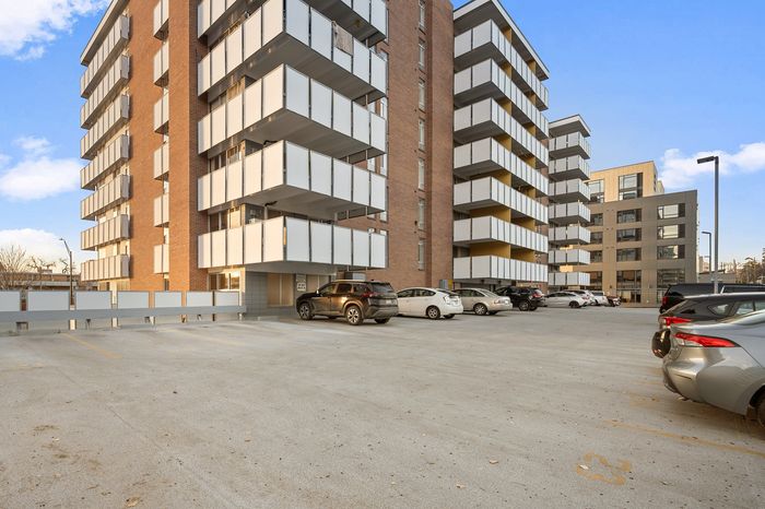 Modern apartment complex with spacious balconies and ample parking, featuring a stylish design against a clear blue sky.