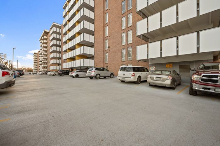 Modern apartment building with spacious parking lot, showcasing sleek white balconies and brick facade under a clear blue sky.