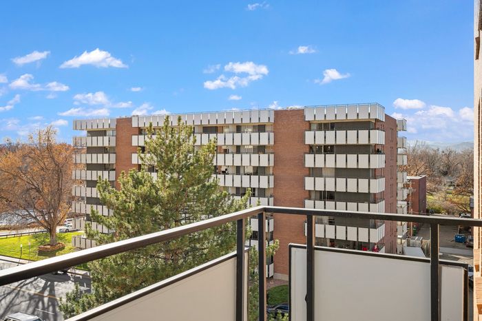 Charming view from a modern apartment balcony overlooking a stylish residential building and lush greenery on a bright day.