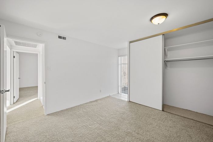 Bright and spacious bedroom with plush carpet, large closet space, and natural light streaming through a window with vertical blinds.