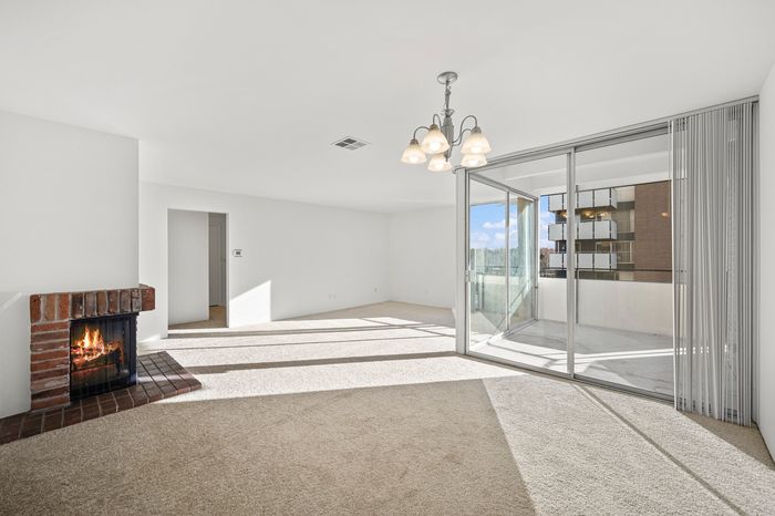 Bright and spacious living room with a modern chandelier, cozy fireplace, and expansive sliding glass doors leading to a sunlit balcony.