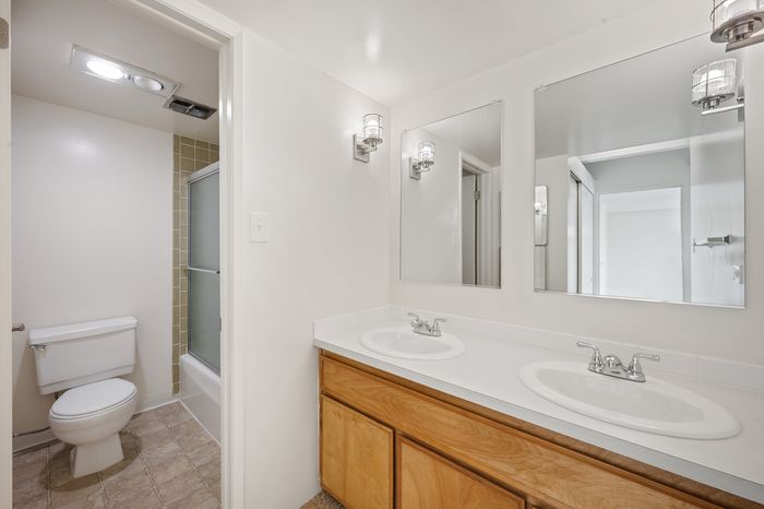 Bright modern bathroom featuring dual sinks, hardwood cabinetry, and a sleek glass-enclosed shower.
