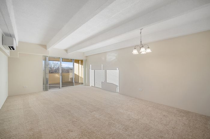 Bright and spacious living room with plush carpeting, elegant ceiling lighting, and large glass doors leading to a private balcony with a scenic view.