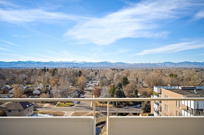 Breathtaking balcony view showcasing a picturesque neighborhood beneath a clear blue sky with majestic mountain ranges in the distance.
