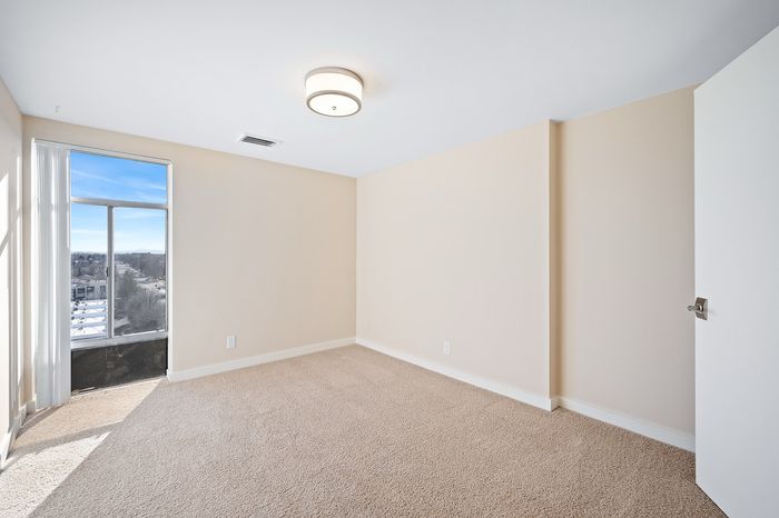 Bright and spacious empty room with plush carpet, large window, and elegant ceiling light, offering stunning views and abundant natural light.