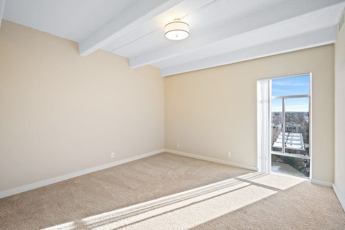 Bright and inviting empty room with plush carpeting and large window offering a stunning city view.