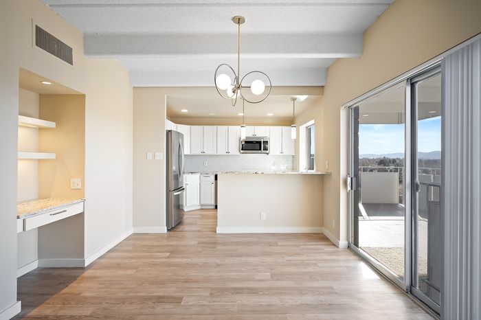 Modern open-concept kitchen and dining area with sleek stainless steel appliances, elegant light fixtures, and large glass doors leading to a scenic balcony view.
