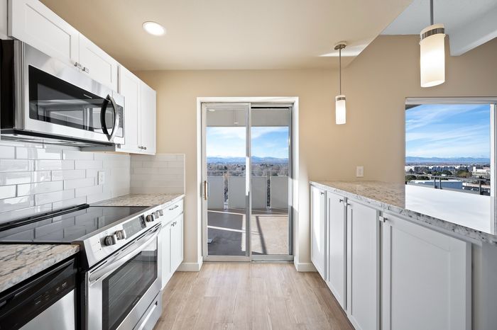 Bright modern kitchen with sleek white cabinetry, marble countertops, and panoramic mountain views through large glass doors.