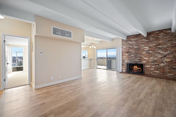 Bright, open-concept living area with a cozy brick fireplace, elegant hardwood floors, and stunning views from the large balcony windows.