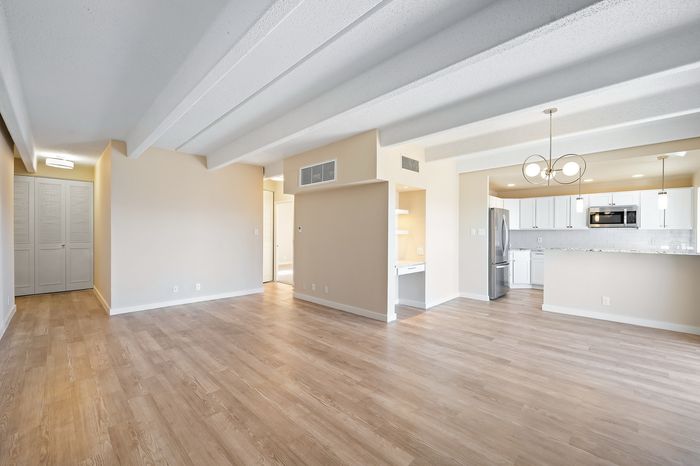 Bright open-plan living area featuring modern kitchen, elegant light fixtures, and spacious wood flooring.