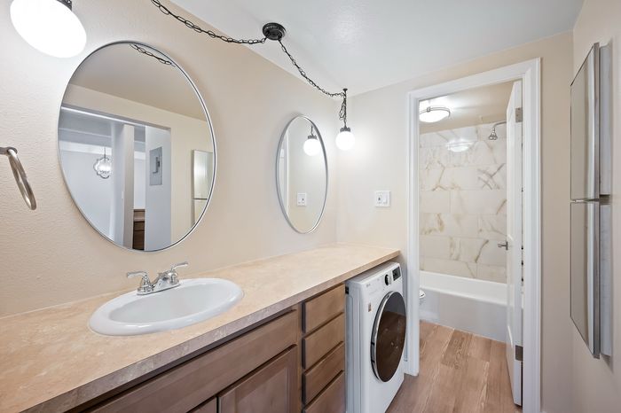 Modern bathroom featuring elegant oval mirrors, sleek vanity with integrated sink, and convenient washer under counter design.