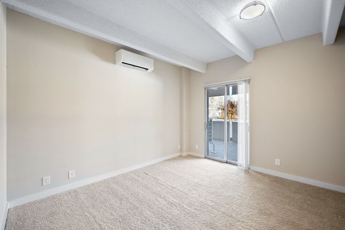 Bright and spacious empty room with beige carpet, large windows, and modern air conditioning, perfect for customization.