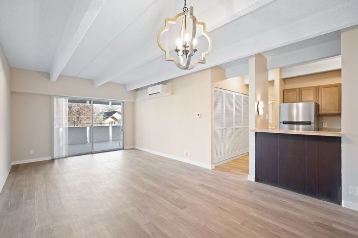 Modern open-concept living room with elegant chandelier, hardwood floors, and sliding glass doors leading to a balcony.