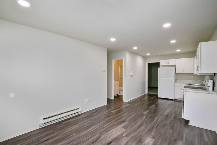 Modern open-plan apartment with sleek dark wood flooring, crisp white kitchen cabinets, and ambient recessed lighting.