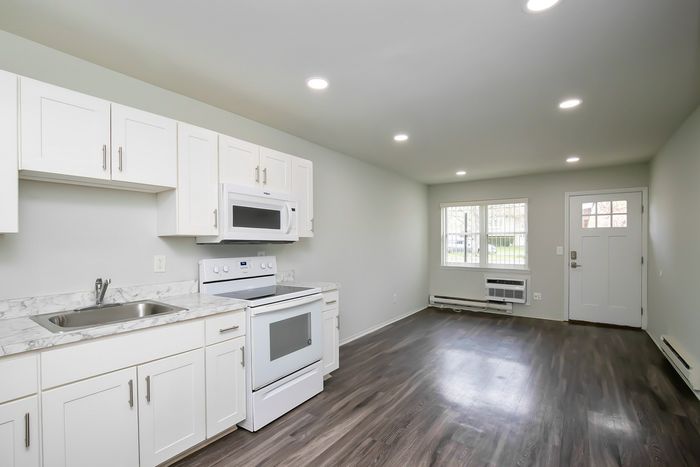 Bright, modern kitchen with sleek white cabinets, marble countertops, and stainless steel appliances flowing into a cozy open-concept living area with hardwood floors.
