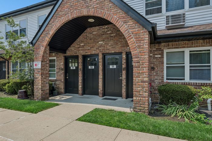 Charming brick facade entrance with three sleek black doors and lush green landscaping, showcasing modern apartments.
