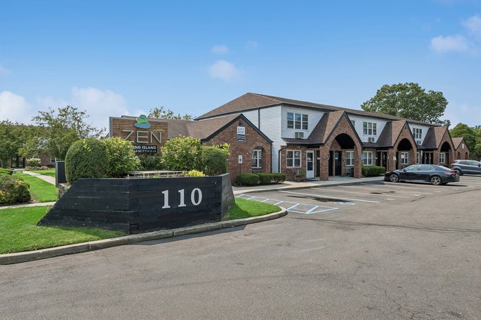 Charming brick apartment complex with modern signage and well-maintained landscaping at Zen Long Island, Amityville, showcasing serene and stylish living.