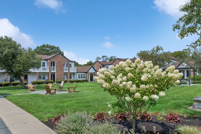 Charming apartment complex with brick facades and lush landscaping featuring blooming hydrangeas and inviting outdoor seating under a bright blue sky.