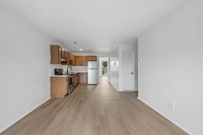 Inviting modern kitchen with sleek wood cabinetry, stainless steel appliances, and open layout leading to a sunlit room, perfect for entertaining.