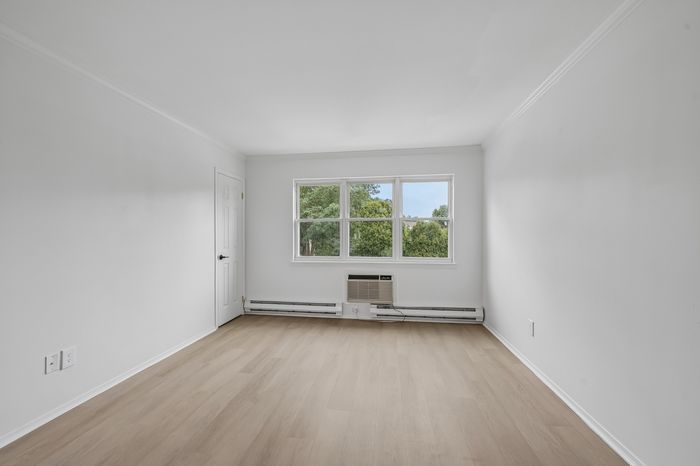Bright, unfurnished room with elegant wooden flooring, large windows showcasing lush greenery, and fresh white walls.
