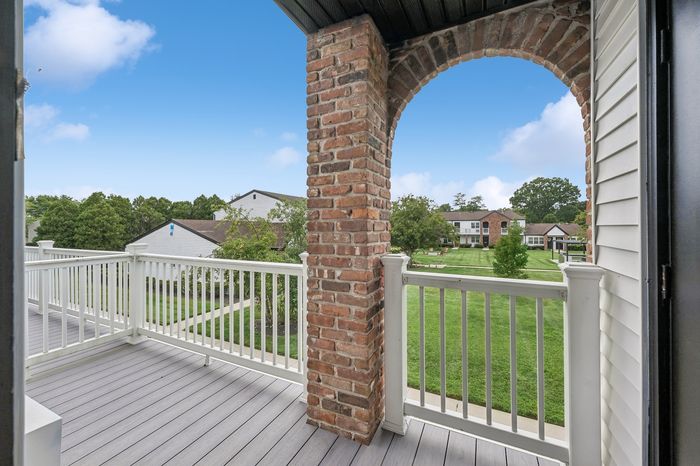 Charming balcony view featuring a classic brick arch, pristine white railing, and lush green community lawns under a bright blue sky.