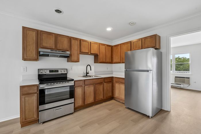 Modern kitchen with sleek stainless steel appliances, elegant wooden cabinets, and spacious countertops leading into a bright living area with a large window.