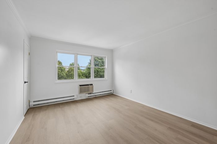 Bright and airy room with fresh white walls, sleek hardwood floors, and large windows overlooking lush greenery.