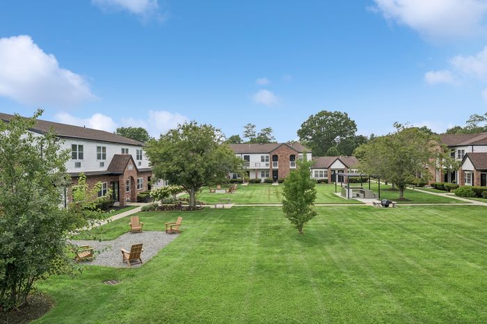 Charming suburban apartment complex with lush green lawns, manicured paths, and inviting outdoor seating areas under a bright blue sky.