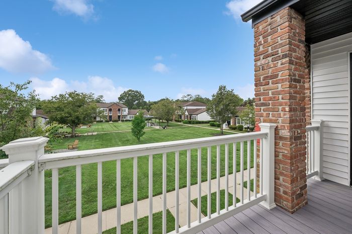 Charming balcony view overlooking lush green lawn and stylish brick homes, ideal for relaxing and enjoying tranquil surroundings.