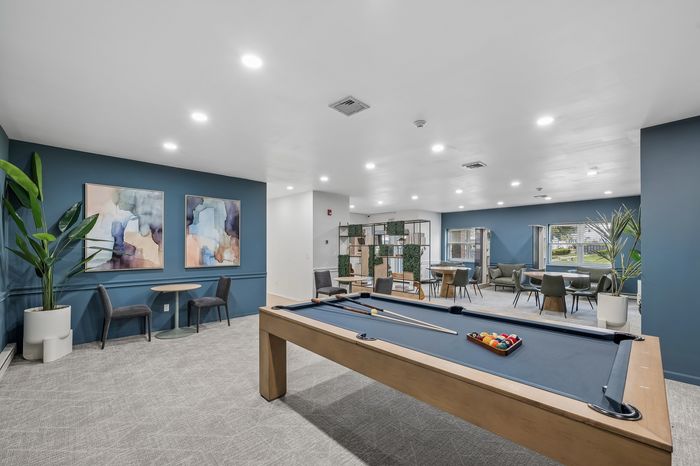 Modern communal lounge with a sleek billiards table, cozy seating area, abstract artwork, and lush greenery, perfect for relaxation and socializing.
