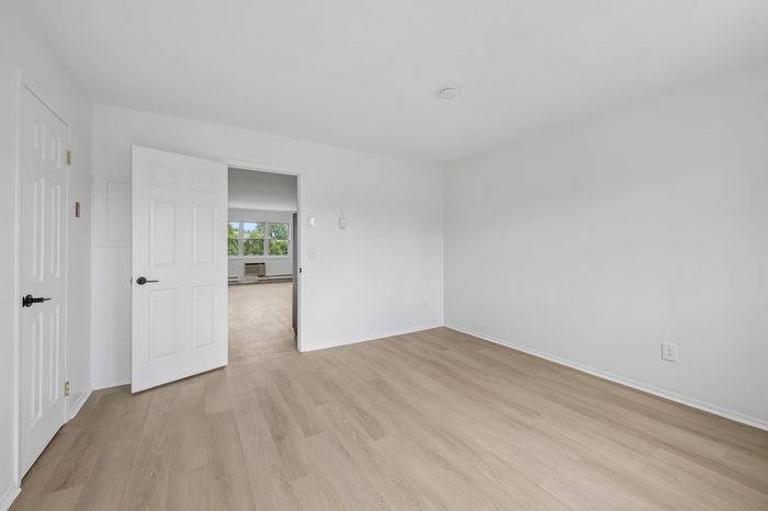 Bright, airy room with elegant hardwood floors and a view into a sunlit living area, perfect for personalizing into a cozy space.