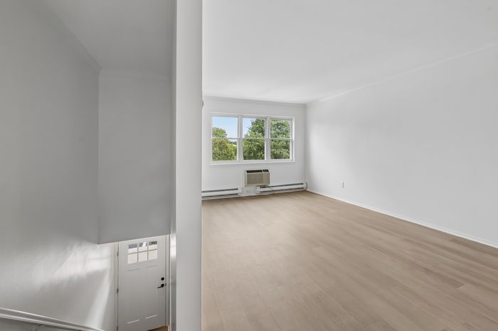 Bright and airy living space with large windows offering scenic views, featuring modern flooring and a sleek entryway.