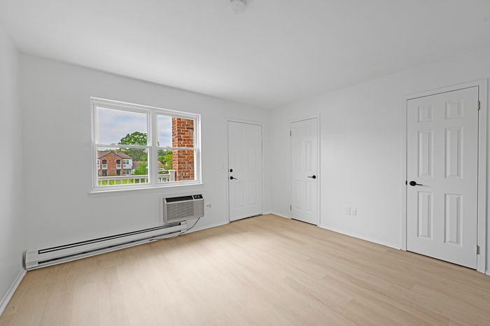 Bright, spacious room featuring sleek hardwood floors, white walls, and ample natural light from a large window.