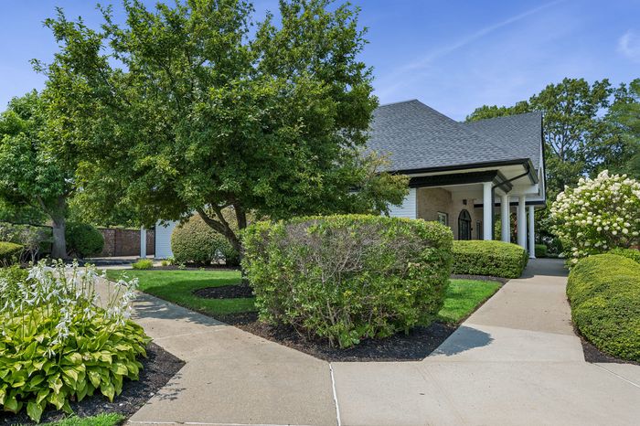 Charming home with lush landscaping, elegant columns, and manicured hedges, offering a serene and inviting atmosphere.