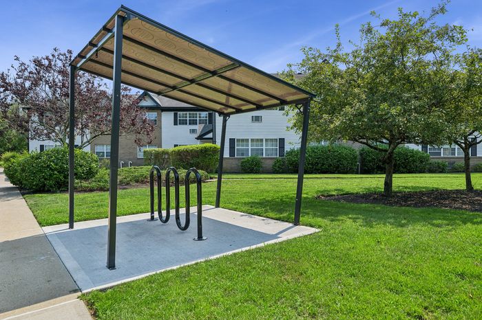 Charming apartment exterior with a modern bike rack and lush, green landscaping under a bright blue sky.