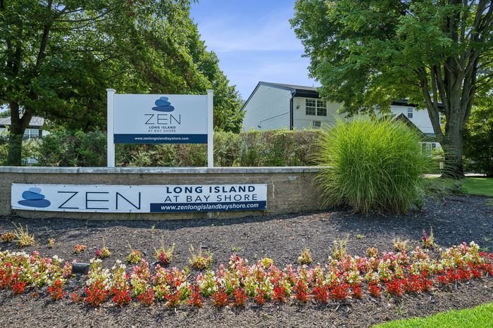 Inviting entrance to Zen Long Island at Bay Shore, surrounded by lush greenery and vibrant flowers, highlighting a serene residential community.