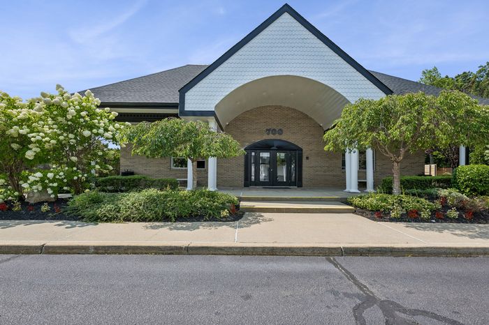 Charming brick building entrance with elegant columns and lush landscaping, creating a welcoming atmosphere.