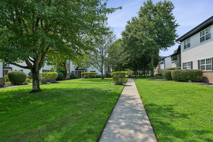 Charming apartment complex with lush green lawns, mature trees, and inviting pathways.