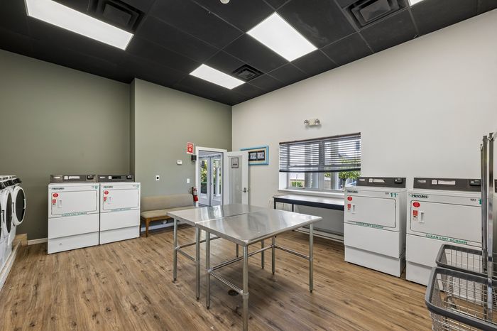 Modern laundry room with spacious folding table, multiple washers and dryers, and stylish wood flooring.